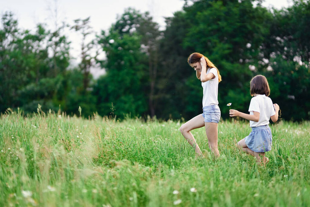 Young mother and her daughter having fun on camomile field - Foto, Imagen
