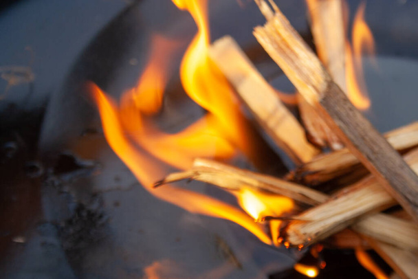 Έναρξη πυρκαγιάς για κάρβουνο Grill. Βραχίονας με μακριά μανίκια που βάζει φωτιά από κοντά. Φωτεινές φλόγες και καμένο ξύλο. - Φωτογραφία, εικόνα
