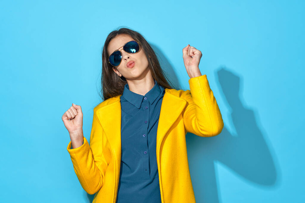 Young beautiful woman in sunglasses dancing    in studio isolated on blue background  - Foto, afbeelding