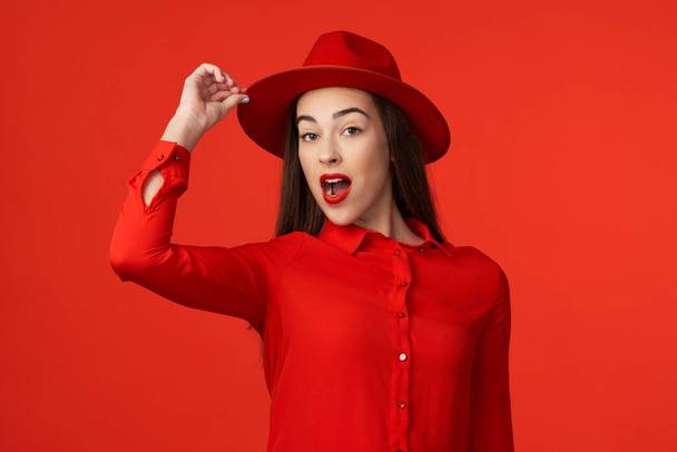 Studio shot. Young beautiful woman in red   wearing hat isolated on red background - Zdjęcie, obraz