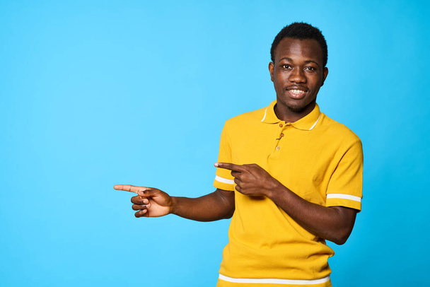 Jeune homme africain pointant isolé sur fond bleu - Photo, image