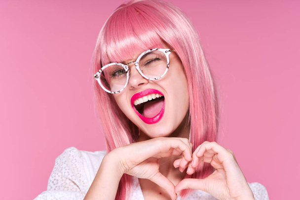 Jeune femme en perruque rose et lunettes clignant sur fond rose - Photo, image