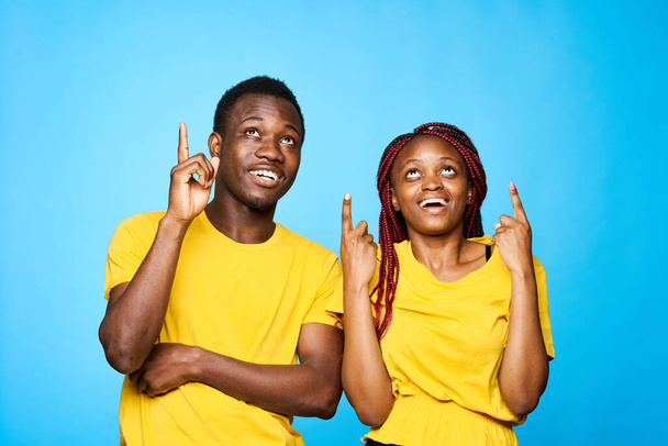 young beautiful couple pointing up  in studio on blue background - Фото, изображение