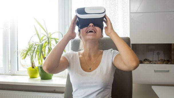 Portret uśmiechniętej podekscytowanej dziewczyny siedzącej w domu i używającej okularów VR - Zdjęcie, obraz
