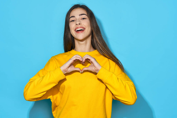 Young beautiful woman  showimg heart gesture   in studio isolated on blue background  - Foto, immagini