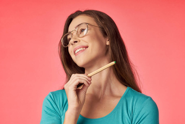 young beautiful woman posing with pencil  in studio on coral background               - Photo, Image