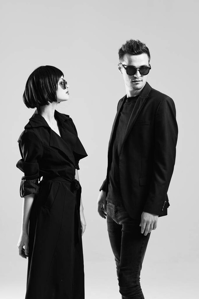 Young beautiful couple in sunglasses posing in studio. Black and white.    - Фото, изображение