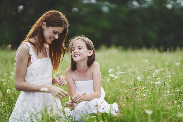 Young mother and her daughter having fun on camomile field - 写真・画像