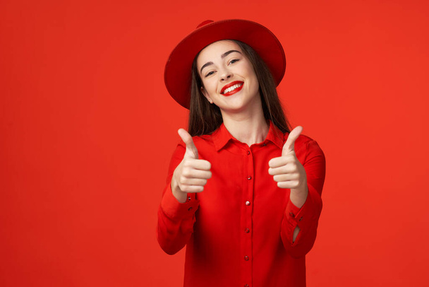 Studio shot. Young beautiful woman in red  with thumbs up  isolated on red background - Photo, Image