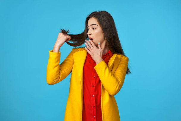 Young woman in yellow jacket  looking on her hair  on  blue background. - Foto, Imagem