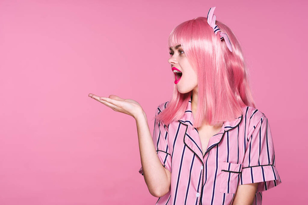Молодая женщина в розовом парике показывает что-то на розовом фоне - Фото, изображение