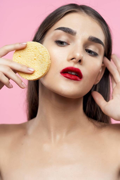 Skincare and beauty. Portrait of young beautiful woman cleaning her skin with sponge on pink background - Photo, Image