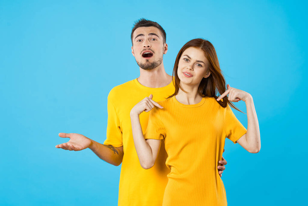 mladý pohledný muž a žena ukazující tričko v ateliéru na modrém pozadí  - Fotografie, Obrázek