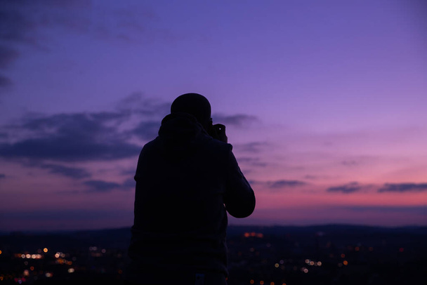 Photographer taking photos of colorful sunset on Bila Hora with amazing view on city Brno Czech Republic pink and orange colors with many clouds and city lights - Photo, image