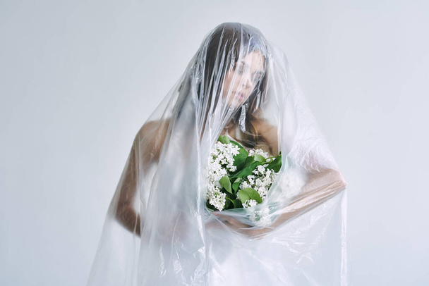 Young woman under plastic sheeting holding flowers. Ecology concept - Foto, Bild