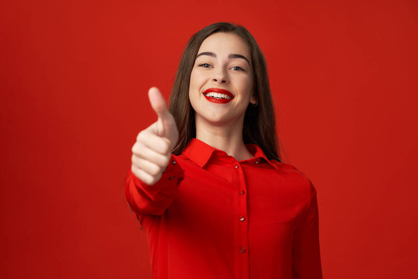 Studio shot. Young beautiful woman in red with thumb up   isolated on red background - Φωτογραφία, εικόνα