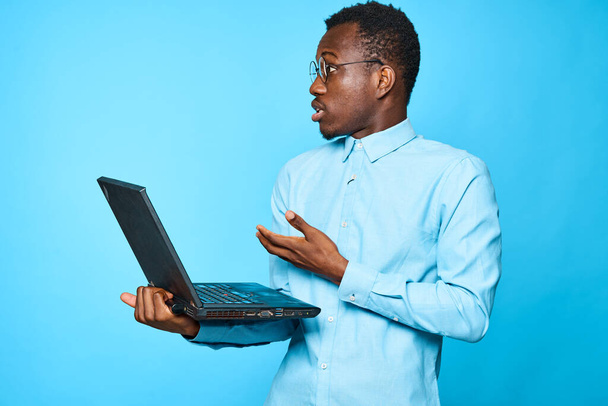 Νεαρός Αφρικανός επιχειρηματίας που κρατά φορητό υπολογιστή απομονωμένο σε μπλε φόντο - Φωτογραφία, εικόνα