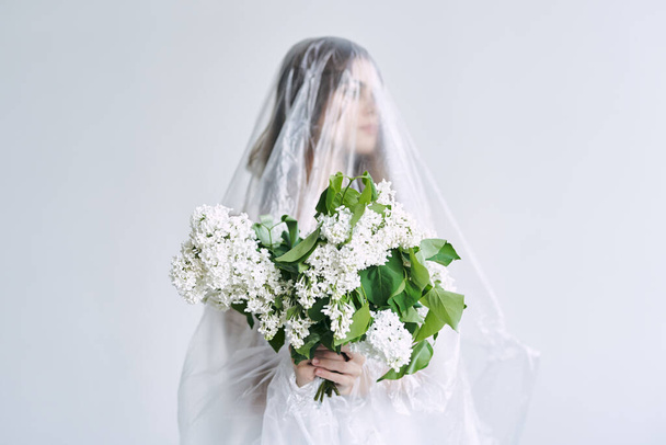 young woman covered with polyethylene holding flowers - Foto, Imagem