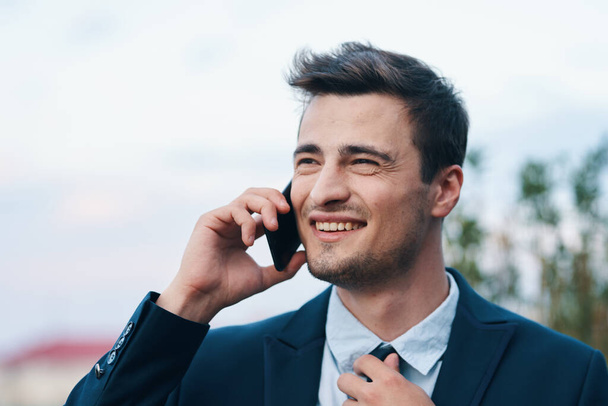 Молодий гарний усміхнений бізнесмен зі смартфоном
  - Фото, зображення