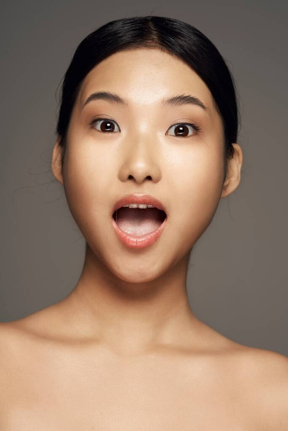 sorprendido joven asiático mujer posando sobre gris fondo
 - Foto, imagen