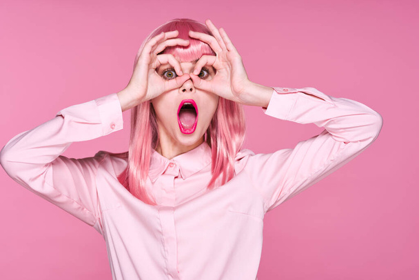 Молодая женщина в розовом парике делает очки на розовом фоне - Фото, изображение