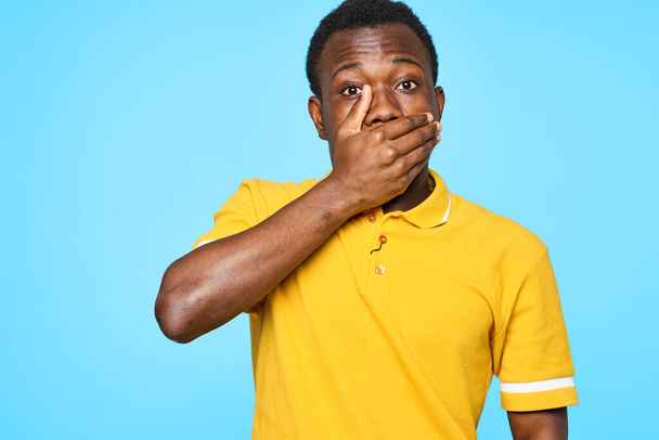 Young african man  closing mouth with hand  isolated on blue background - 写真・画像
