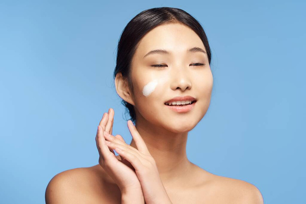 Jovem mulher asiática aplicando hidratante em seu rosto
  - Foto, Imagem