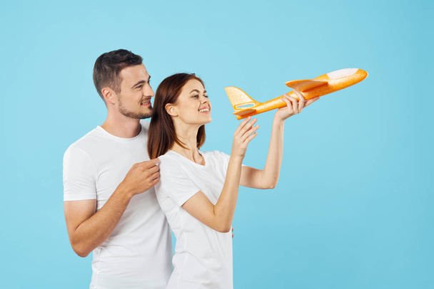 Νεαρό όμορφο ζευγάρι παίζει με κίτρινο παιχνίδι αεροπλάνο σε μπλε φόντο  - Φωτογραφία, εικόνα
