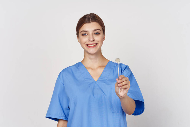 νεαρή νοσοκόμα κρατώντας οδοντικό εργαλείο καθρέφτη. Φωτογραφία στούντιο - Φωτογραφία, εικόνα