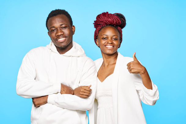 young beautiful couple posing in studio on blue background. woman with thumb up - Fotó, kép