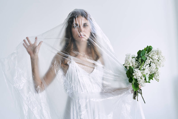 Young woman under plastic sheeting holding flowers. Ecology concept - Фото, зображення