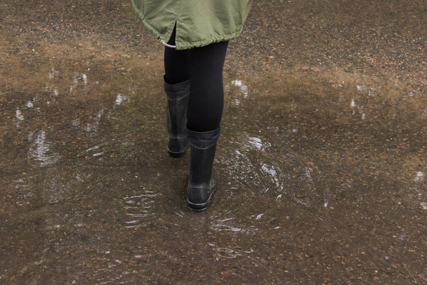persoon staat in een plas op een overstroomde straat in rubberen laarzen, close-up zicht op zijn voeten. het regen- en moessonseizoen.Het concept van kinderrecreatie, wandelingen in alle weersomstandigheden, de gezondheid van het kind - Foto, afbeelding
