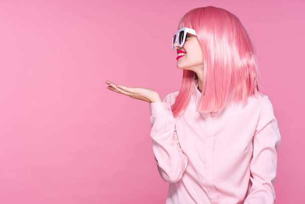 Νεαρή γυναίκα με ροζ περούκα δείχνει παλάμη σε ροζ φόντο - Φωτογραφία, εικόνα