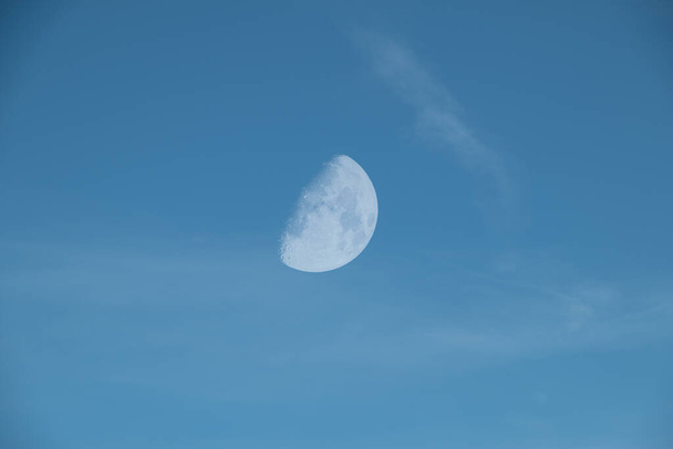 Céu azul com nuvens estranhas sussurradas e uma meia lua ondulante ou minguante
. - Foto, Imagem