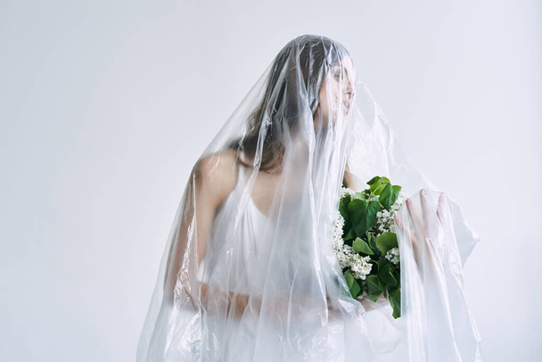 Young woman under plastic sheeting holding flowers. Ecology concept - Photo, Image