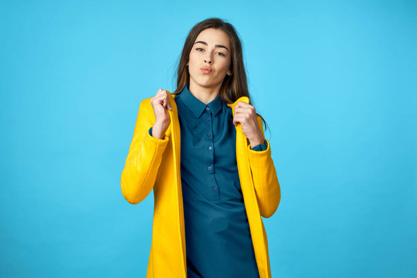 young beautiful woman in yellow jacket showing kiss    in Studio with blue Background. - Fotó, kép