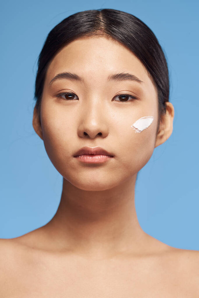Молодая азиатка наносит увлажняющий крем на лицо
  - Фото, изображение