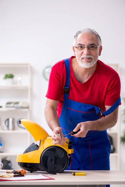 Old male contractor repairing vacuum cleaner indoors - Photo, Image