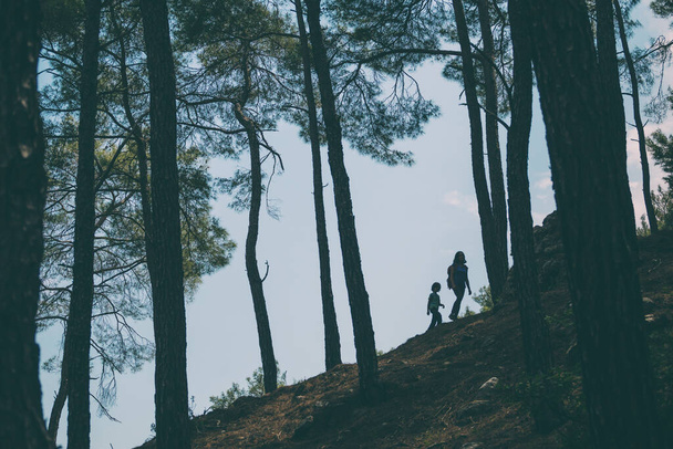 Žena kráčí se svým synem lesem, Chlapec se svou matkou jít turistiku, Silueta ženy s batohem a dítě proti obloze, Cestování s dětmi, Horská stezka, Den matek. - Fotografie, Obrázek