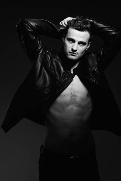 Portrait of young handsome man in black leather jacket posing in studio. Black and white   - Photo, Image