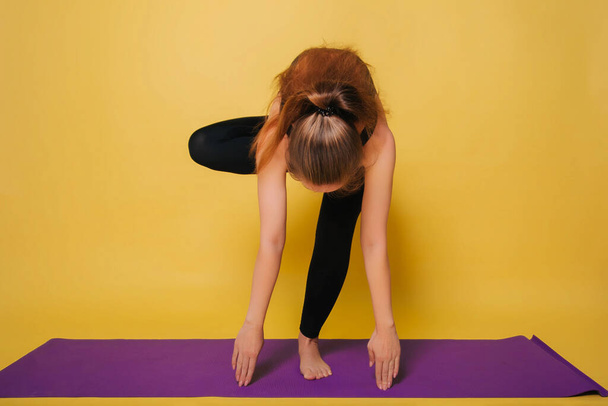 Atlético, bela menina praticando ioga, fazendo uma pose. Use sportswear preto em um fundo amarelo liso
, - Foto, Imagem