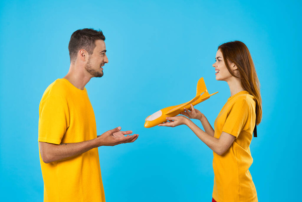 Genç ve güzel bir çift mavi arka planda sarı oyuncak uçakla oynuyor.  - Fotoğraf, Görsel