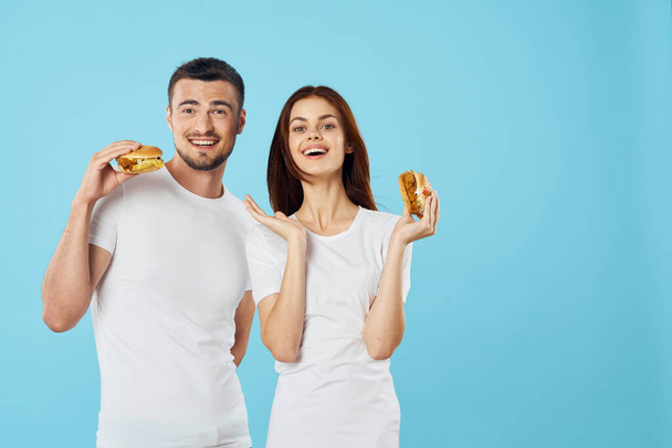 Young beautiful couple eating hamburgers. Studio shot - Photo, Image