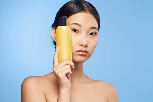 Studio shot. Young asian woman with beauty product on blue - Photo, Image