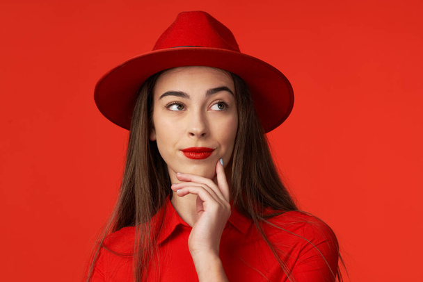 Studio shot. Young beautiful woman in red thinking   isolated on red background - Photo, Image
