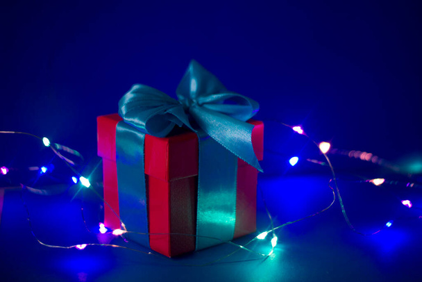confezione regalo rossa con nastro blu su sfondo blu con luci colorate
 - Foto, immagini
