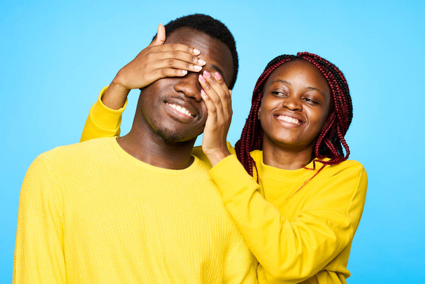young beautiful couple posing in studio on blue background. woman closing man's eyes  - Photo, Image