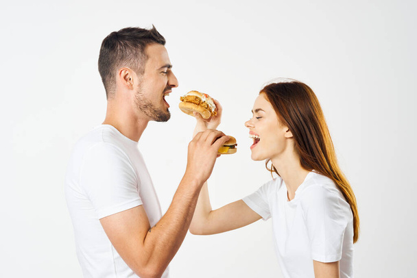 Young beautiful couple eating hamburgers. Studio shot - Foto, imagen