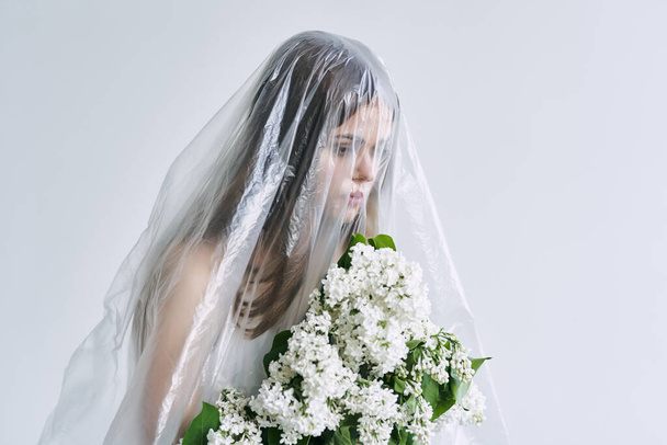 Young woman under plastic sheeting holding flowers. Ecology concept - Fotoğraf, Görsel