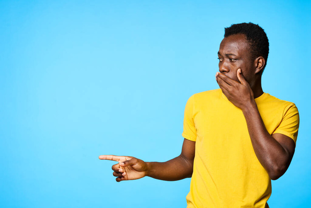 Jeune homme africain confus pointant isolé sur fond bleu - Photo, image